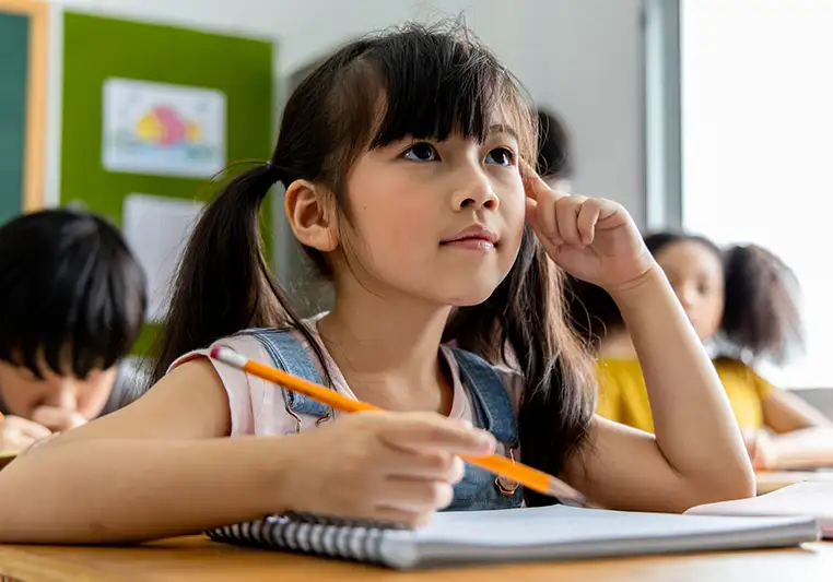 A young girl with pigtails writing in her notebook in a classroom