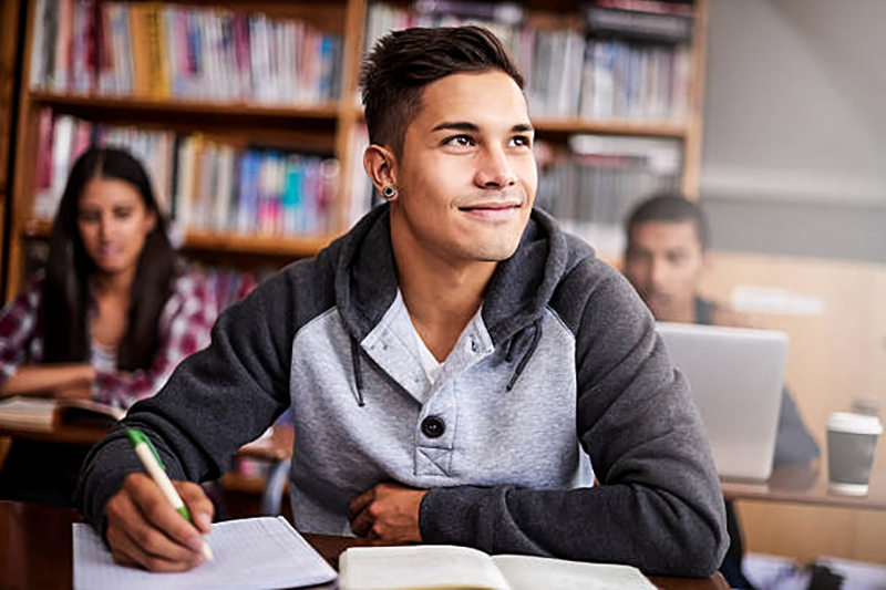 A hispanic teen writing in a notebook in a classroom