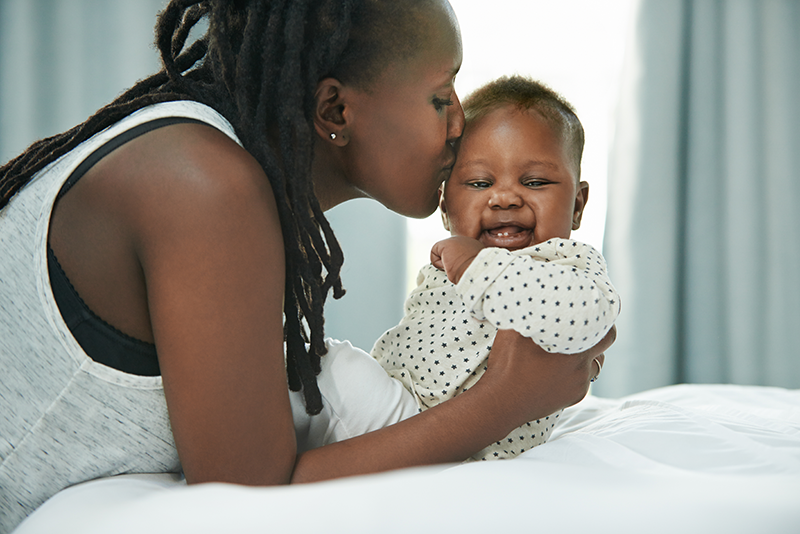 An African American mom kissing her newborn baby
