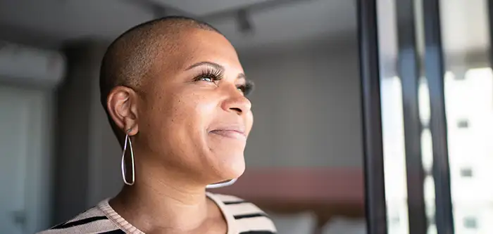 African American woman in a striped shirt smiling and looking off into the distance (700x333 vertical tab)