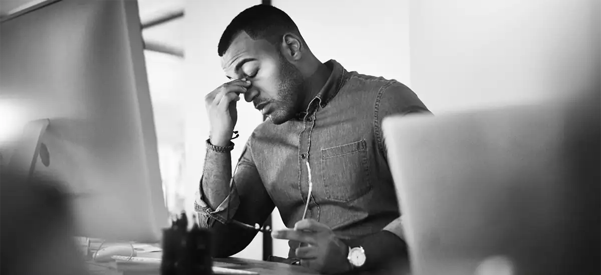 A tired looking man at his computer with his fingers pressed to the bridge of his nose