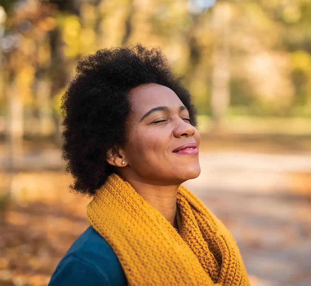 Woman in yellow scarf with closed eyes looking up at the sun