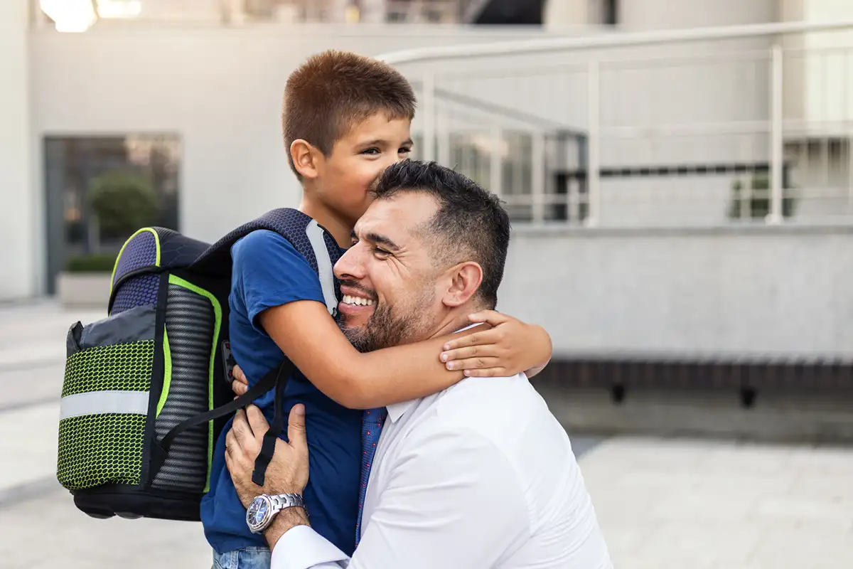A father hugging his son who has a backpack